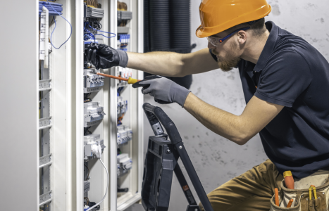 Electrician wiring a domestic consumer unit, illustrating an AiBoost analysis of SEO search demand and click costs for UK electrical firms.
