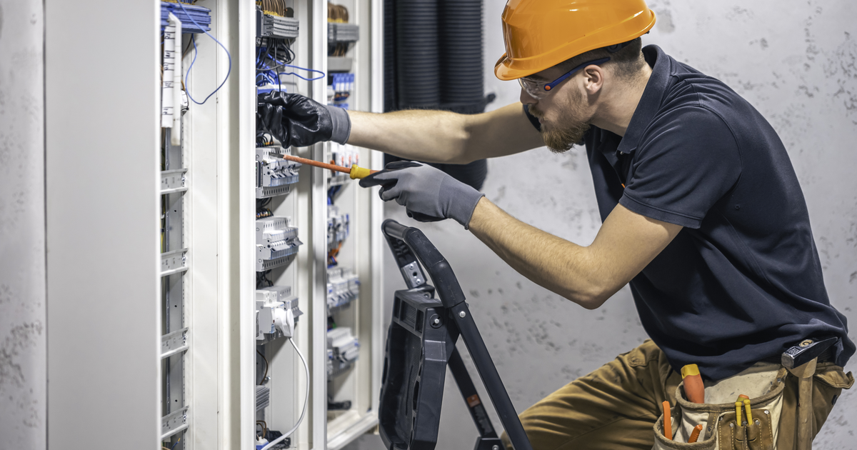 Electrician wiring a domestic consumer unit, illustrating an AiBoost analysis of SEO search demand and click costs for UK electrical firms.