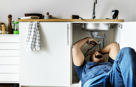 Plumber working under a kitchen sink with tools laid out, illustrating an AiBoost analysis of SEO search demand for UK plumbing businesses.