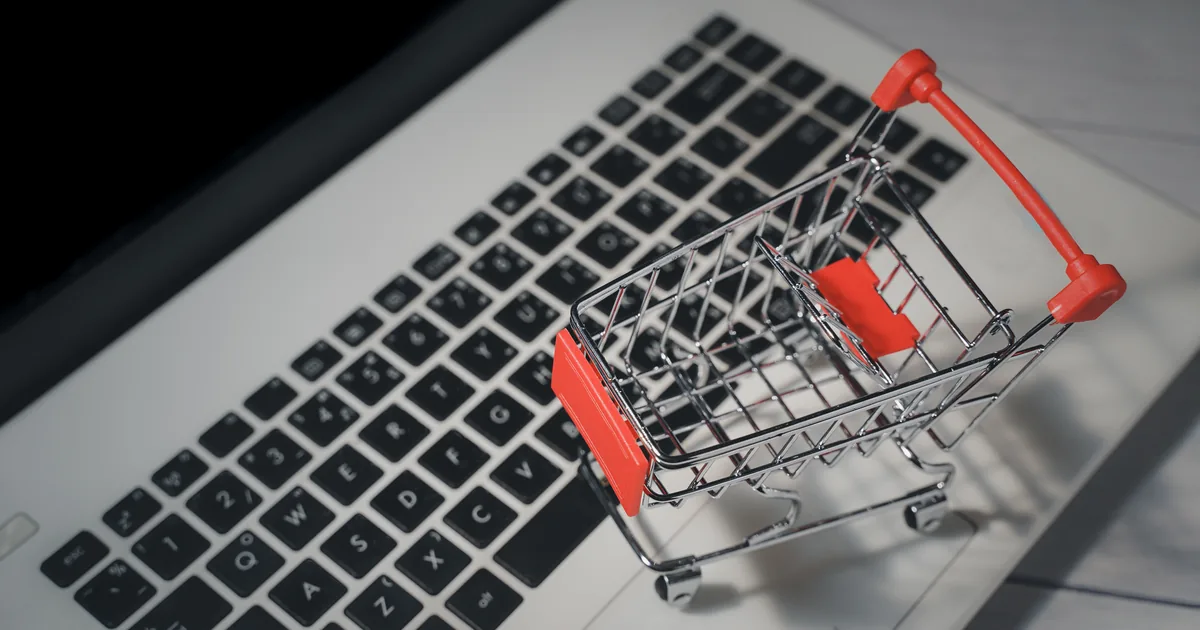 A miniature metal shopping trolley standing on a laptop keyboard, illustrating the cost of ecommerce pay-per-click advertising in the UK.
