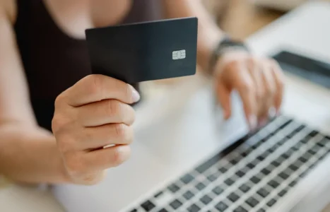 A shopper holding a bank card in one hand while typing card details into a laptop, illustrating ecommerce checkout conversion rate optimisation.
