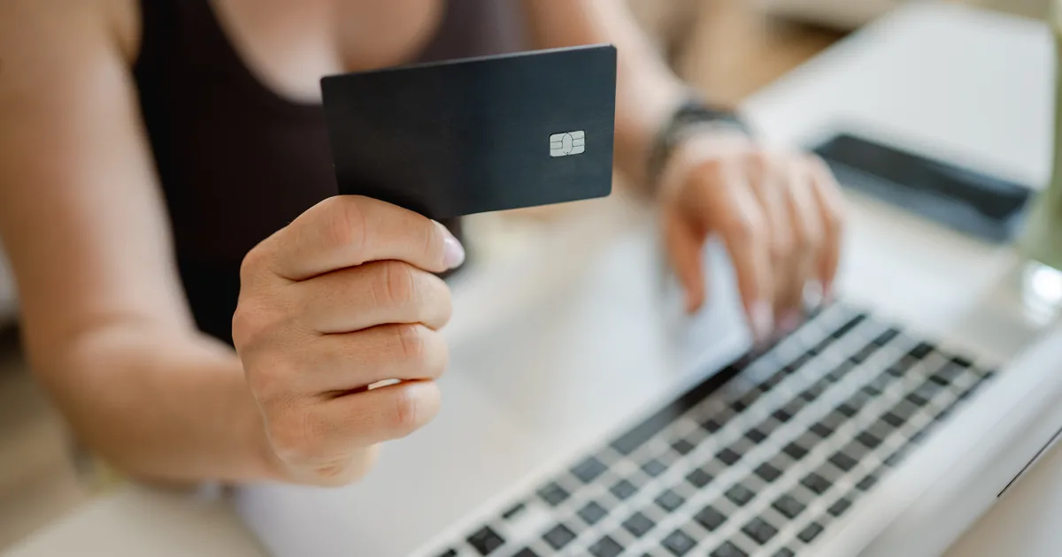 A shopper holding a bank card in one hand while typing card details into a laptop, illustrating ecommerce checkout conversion rate optimisation.