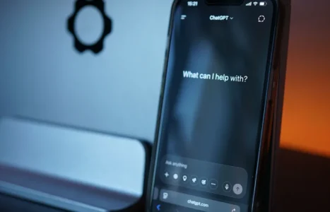A smartphone on a desk stand showing the ChatGPT app with the prompt What can I help with.