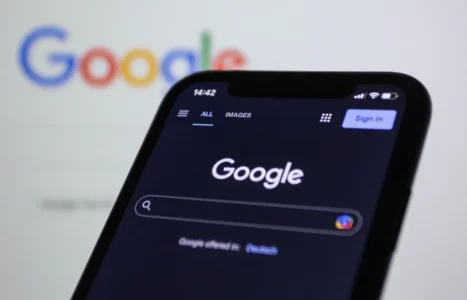 A smartphone showing the Google search page held in front of a large Google logo.