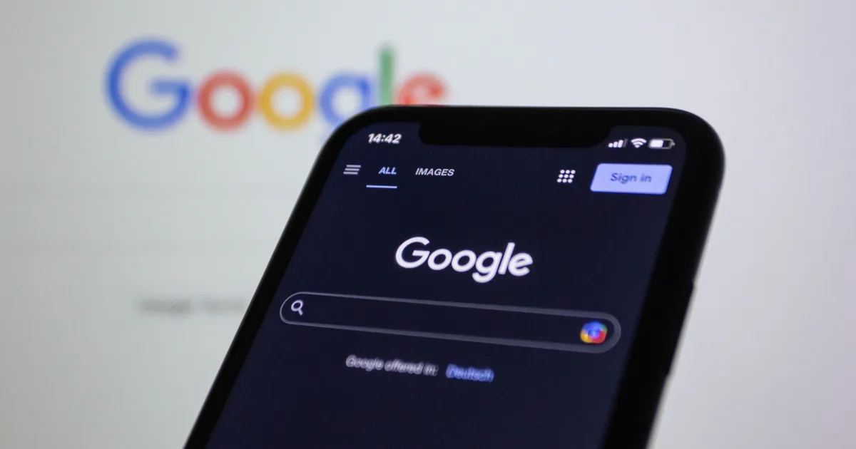 A smartphone showing the Google search page held in front of a large Google logo.